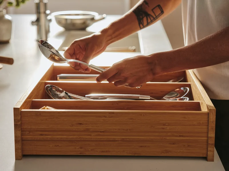 Mains rangeant des ustensiles de cuisine dans un organiseur de tiroir en bambou